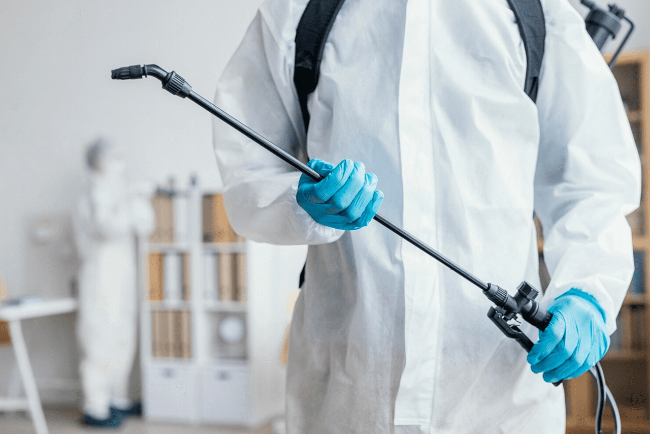 Exterminator wearing protective gear and using a pest control sprayer
